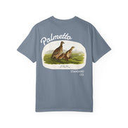 A slate blue short-sleeve t-shirt with a vintage-style graphic on the front. The graphic features an illustration of two prairie chickens in a grassy field, framed by an off-white border with the text 'Palmetta' above and 'STANDARD CO.
